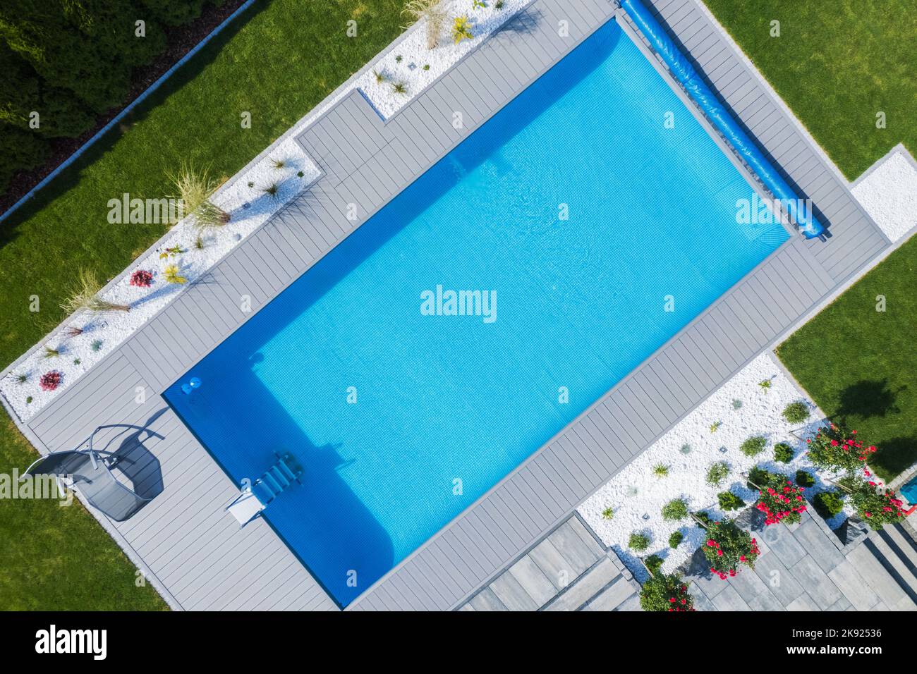 Perfectly Maintained Outdoor Swimming Pool Surrounded by Green Lawn and Landscaped Flower Beds. Residential House Backyard Garden Design. Recreational Stock Photo