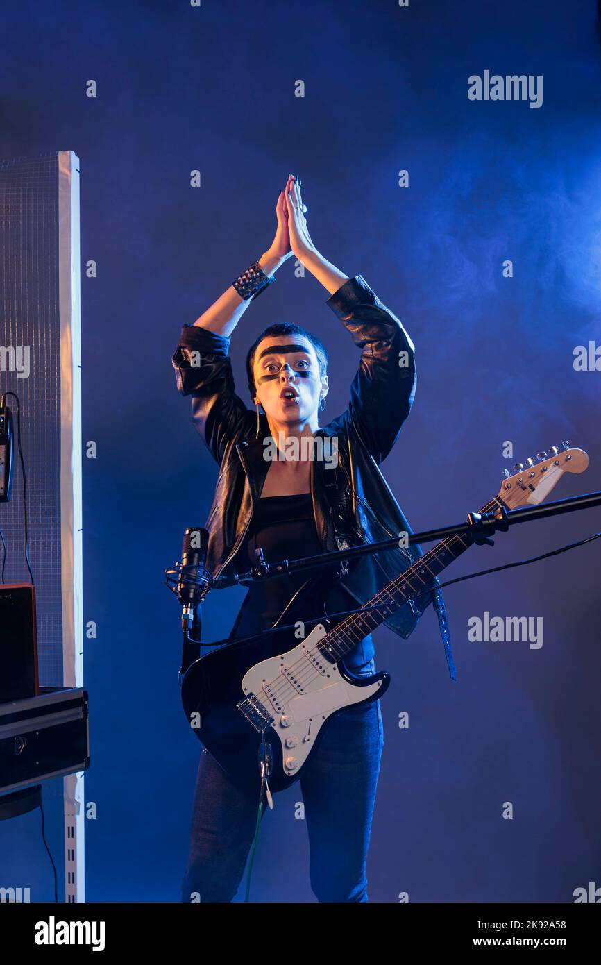 Heavy metal artist clapping hands and doing live rock performance with alternative music. Creating vibe and cool funky atmosphere, singing songs with guitar and wearing leather jacket. Stock Photo