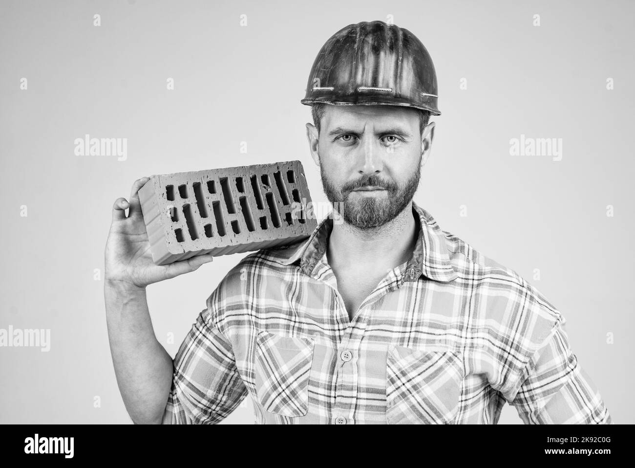 man bricklayer in construction helmet and checkered shirt on building site with brick, brickwork. Stock Photo