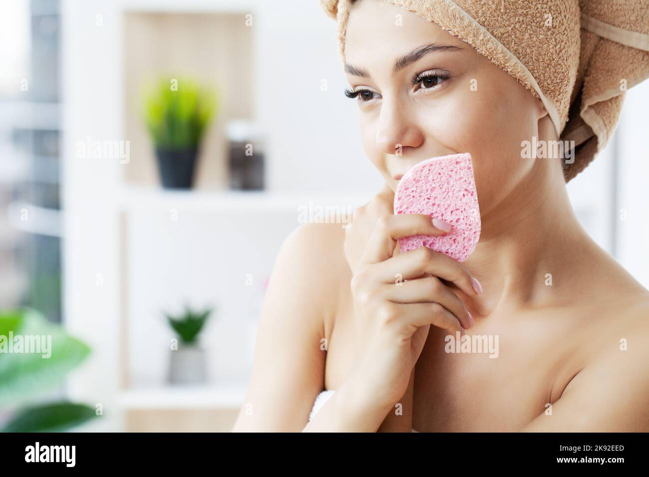 Beautiful young woman is cleaning her face using a cosmetic sponge