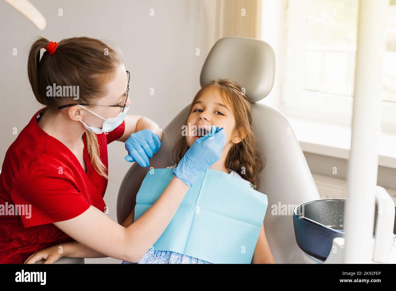 Pediatric dentist examines teeth of child girl for treatment of