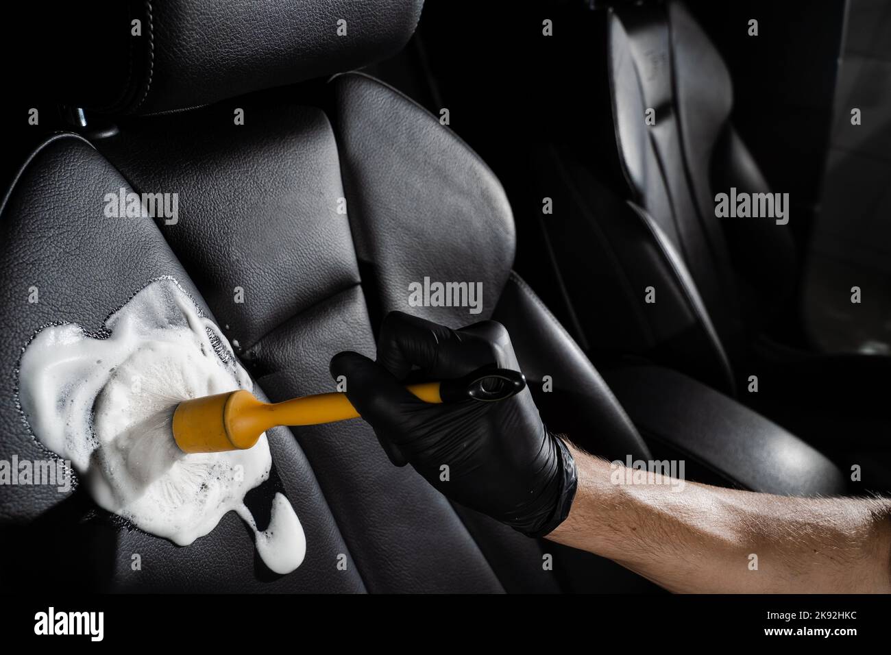 Process of foam and detergent cleaning leather seat using brush. Worker