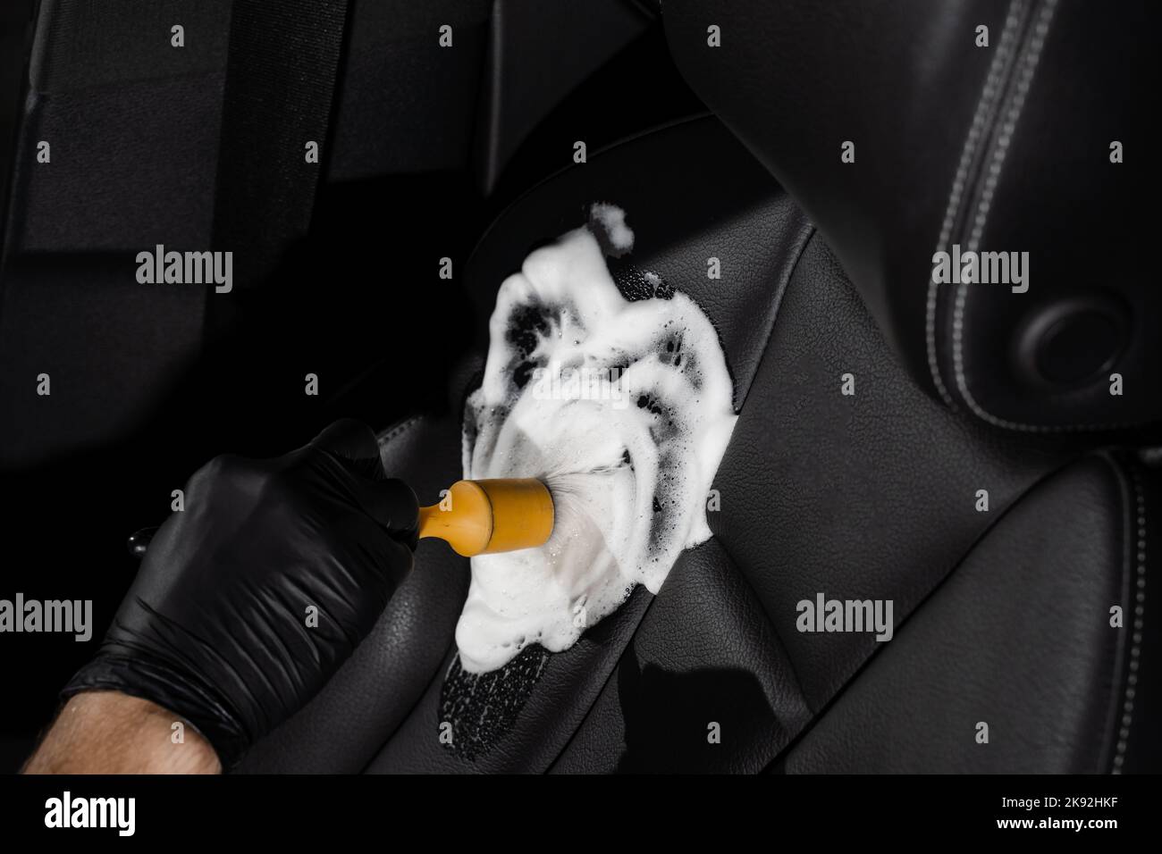 Process of foam and detergent cleaning leather seat using brush. Worker