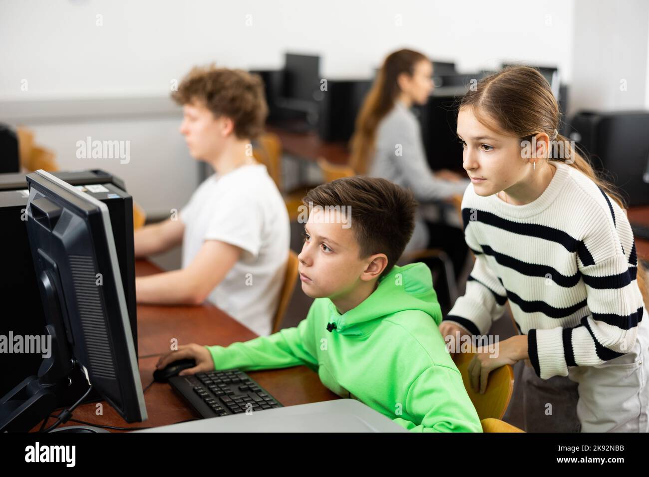 Teen schoolgirl helping focused classmate sitting at computer in class ...