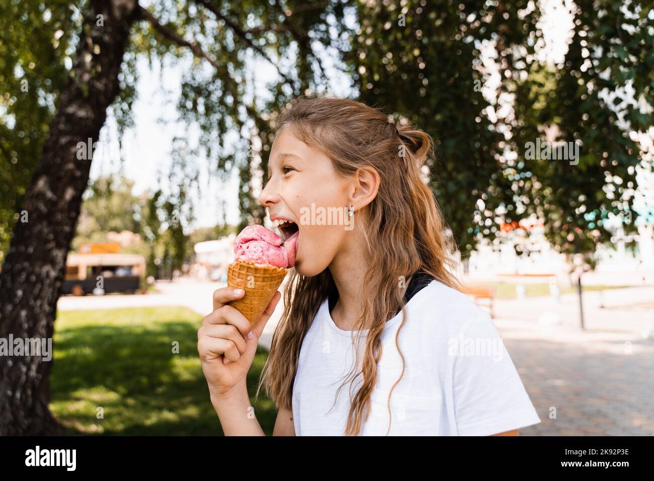 Funny child girl eating ice cream cone in waffle cup. Creative advert for ice cream stand and
