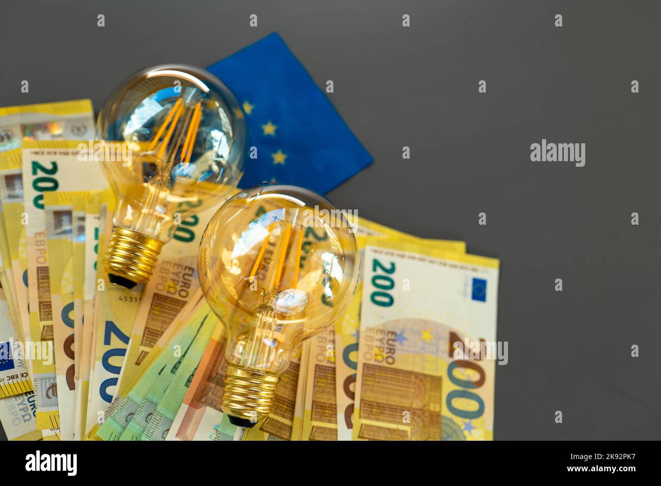 Electricity cost. Light bulbs and euro bills and the EU flag on a dark gray background.Energy crisis .Rising electricity prices.Paying electricity Stock Photo