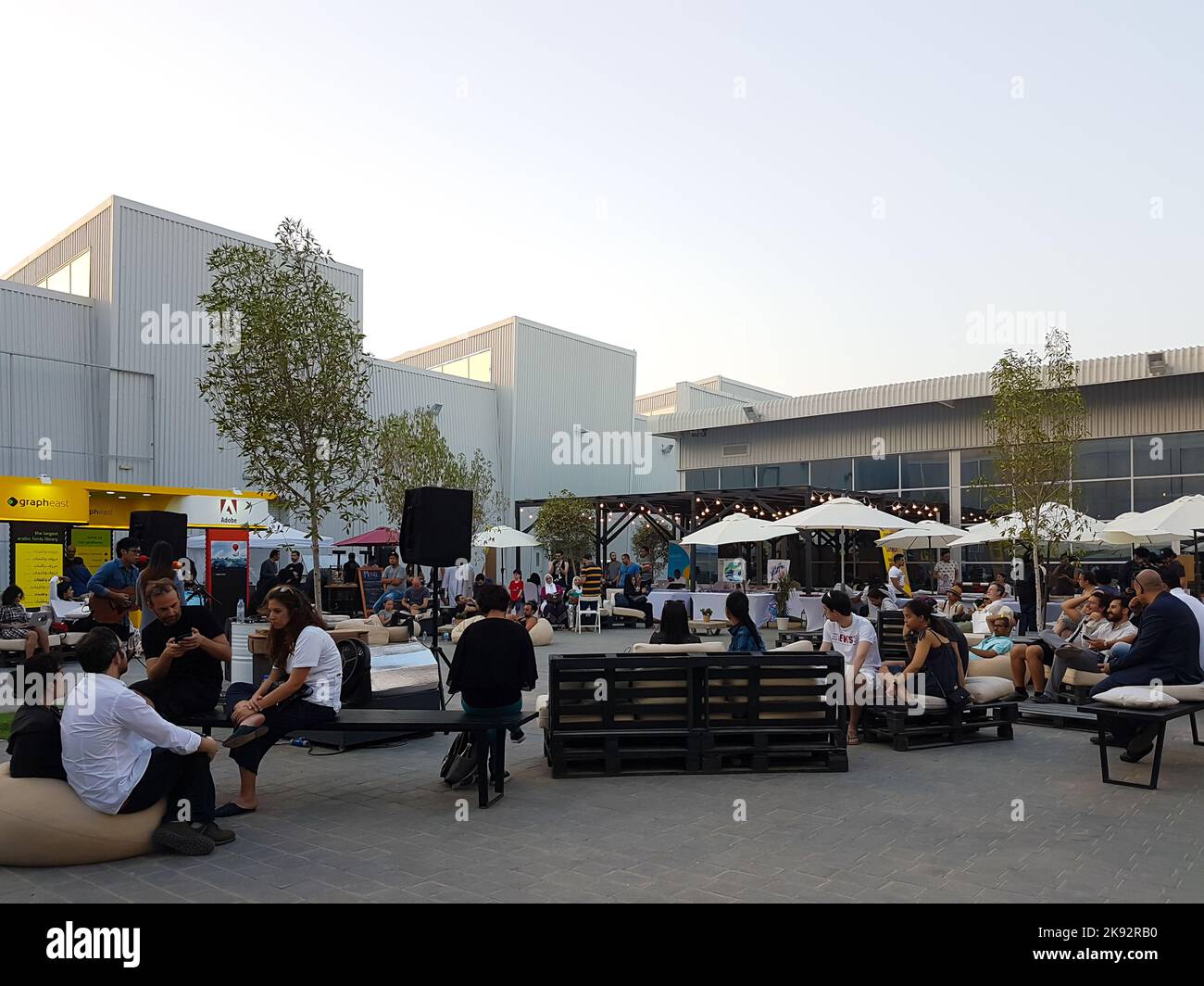 Art Fair in Alserkal Avenue during Art Week. People gathered in outdoor seating with benches, pop-up stalls, and big umbrellas. Urban city day scene. Stock Photo