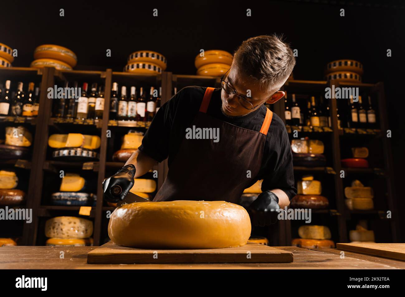 Cheese sommelier cutting yellow cheese wheel cut in half with a knife