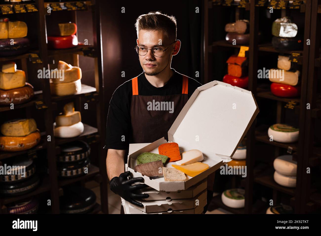 Cheese Sommelier holding many boxex with mix of young Gouda, young goat, lavander cheese and green and red pesto cheeses on the table. Creative idea f Stock Photo