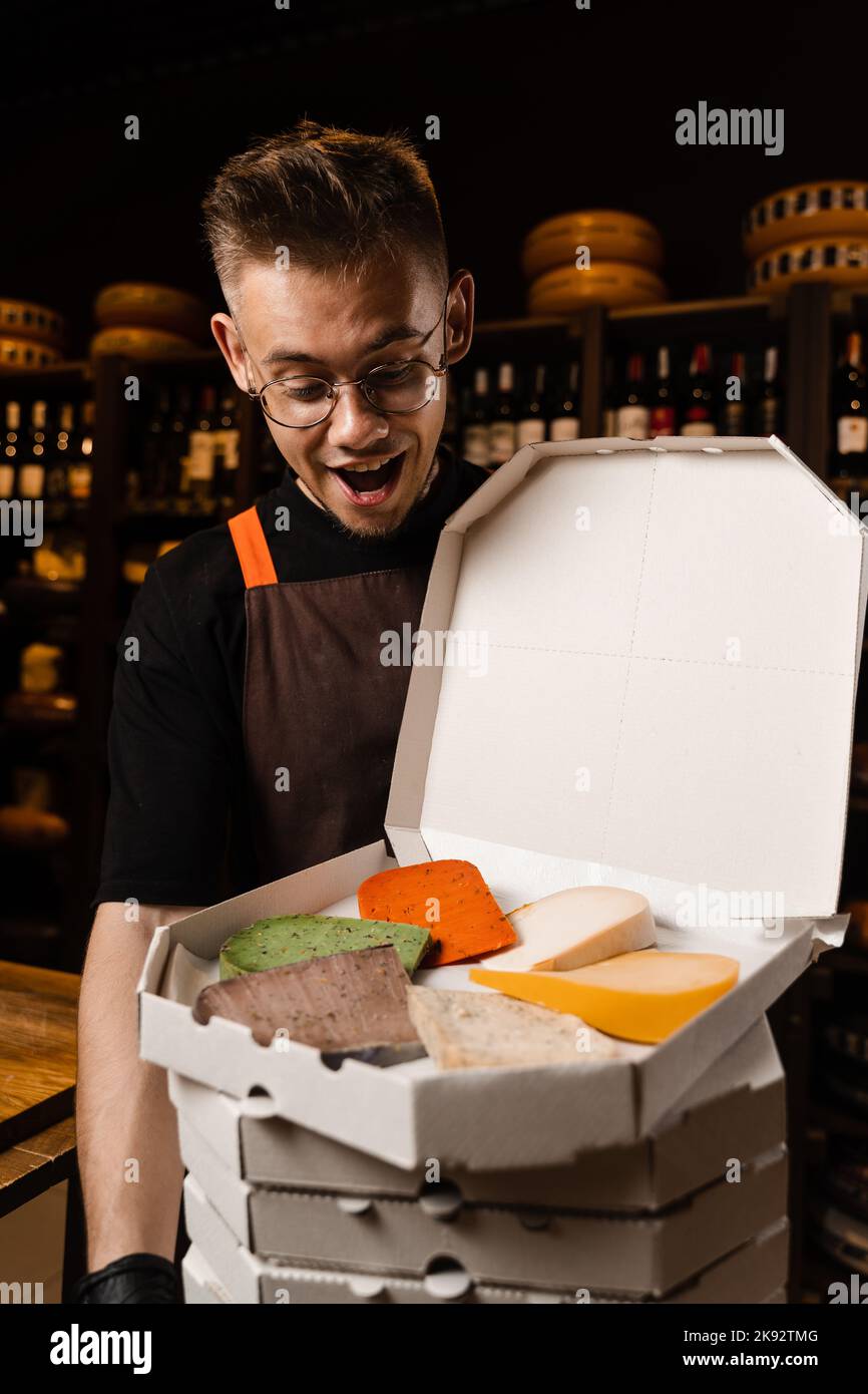 Cheese Sommelier holding many boxex with mix of young Gouda, young goat, lavander cheese and green and red pesto cheeses on the table. Creative idea f Stock Photo