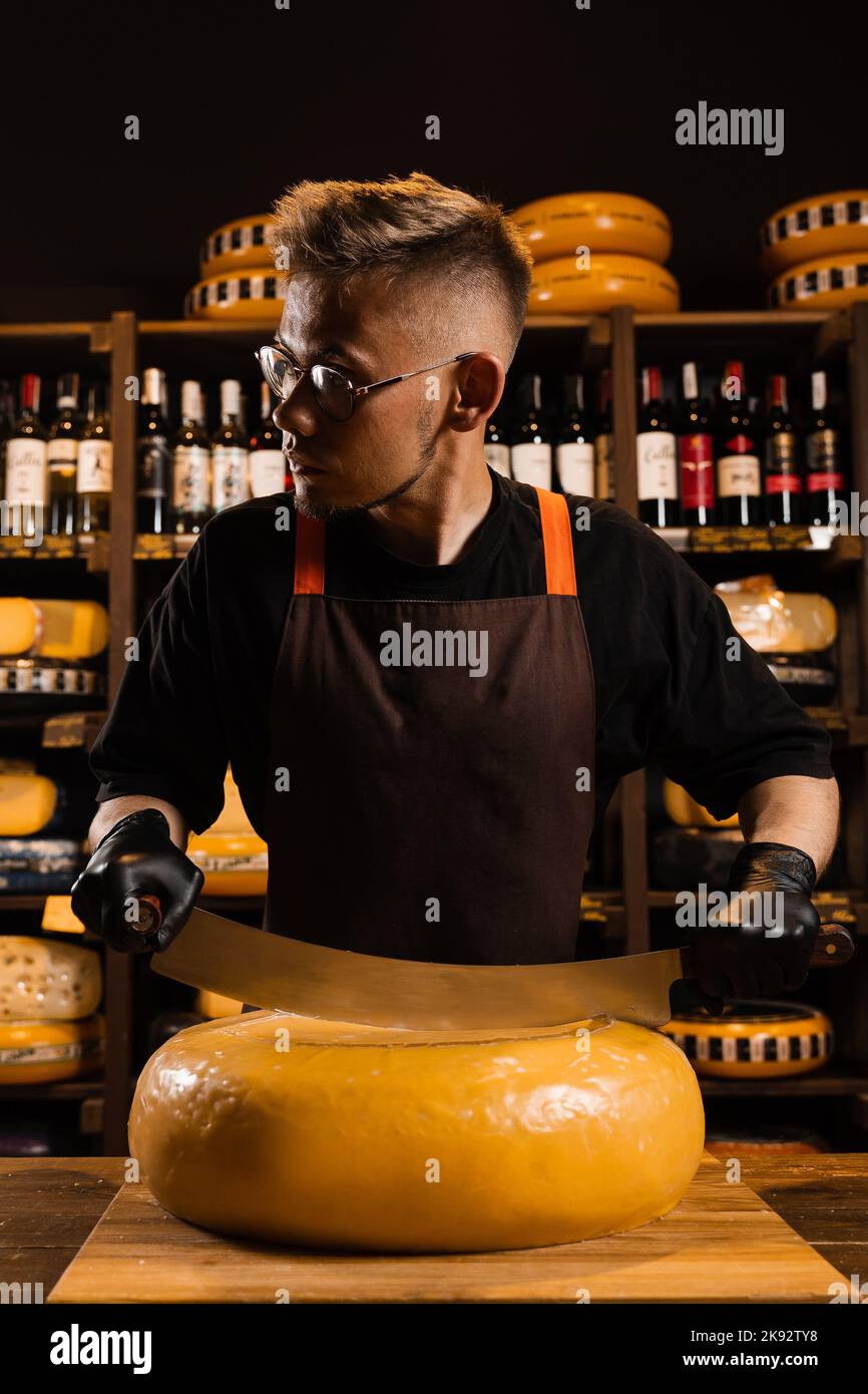 Cheese sommelier cutting yellow cheese wheel cut in half with a knife