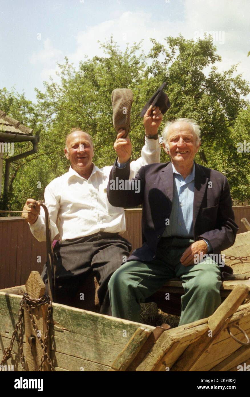 Covasna County, Romania, approx. 2002. Men riding a horse-drawn wagon waving their hats to gesture good bye. Stock Photo