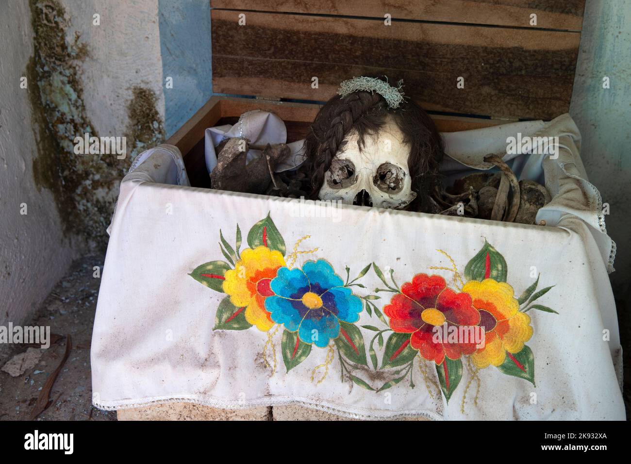 A dried-up skull and bones are seen wrapped in an embroidered white tablecloth bearing the name of the deceased, and placed in a wooden crate inside a niche at the cemetery in Pomuch, Campeche state, Mexico on October 22, 2022. Every year in preparation for Hanal Pixán, the Mayan Day of the Dead celebration, members of the Pomuch community in southeastern Mexico extract bones from their niches and carefully clean them – an ancestral tradition seen as a gesture of love and a way to get closer to deceased family members. This ritual, which in Mayan is known as Choo Ba’ak, can be done for the fir Stock Photo