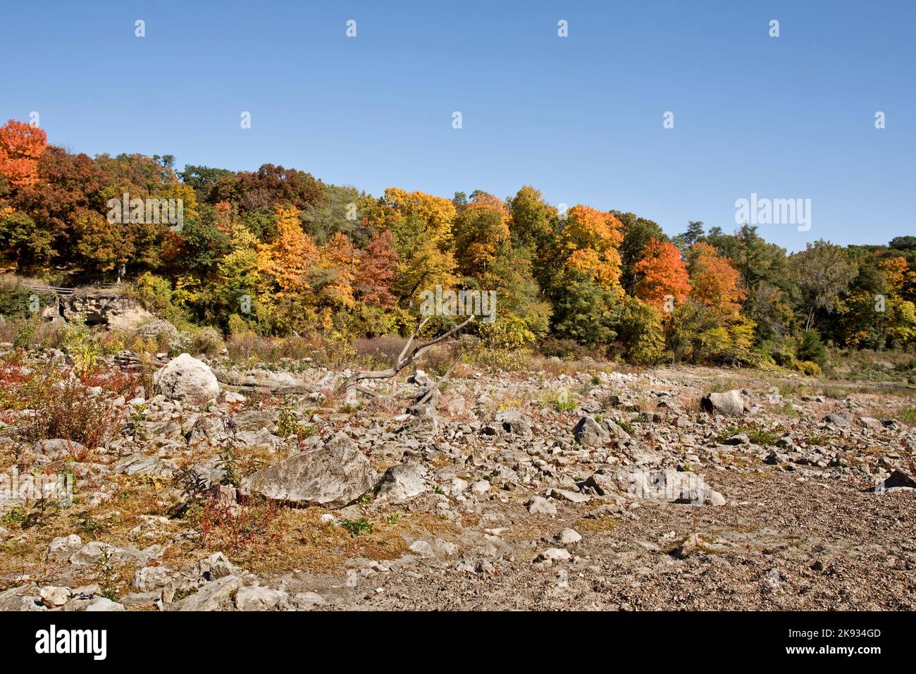 Autumn landscape with rocky ground in the foreground and fall foliage in the trees and blue sky in the background. Stock Photo