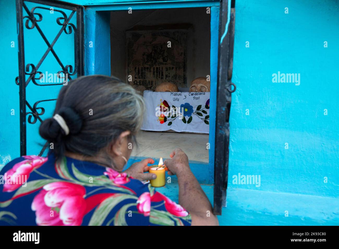 A woman lighting a candle on the niche of her deceased grandparents from the Uitz Poot family at the cemetery of Pomuch, Campeche state, Mexico on October 22, 2022. Every year in preparation for Hanal Pixán, the Mayan Day of the Dead celebration, members of the Pomuch community in southeastern Mexico extract bones from their niches and carefully clean them – an ancestral tradition seen as a gesture of love and a way to get closer to deceased family members. This ritual, which in Mayan is known as Choo Ba’ak, can be done for the first time when a person has been dead for three years. Pomuch and Stock Photo