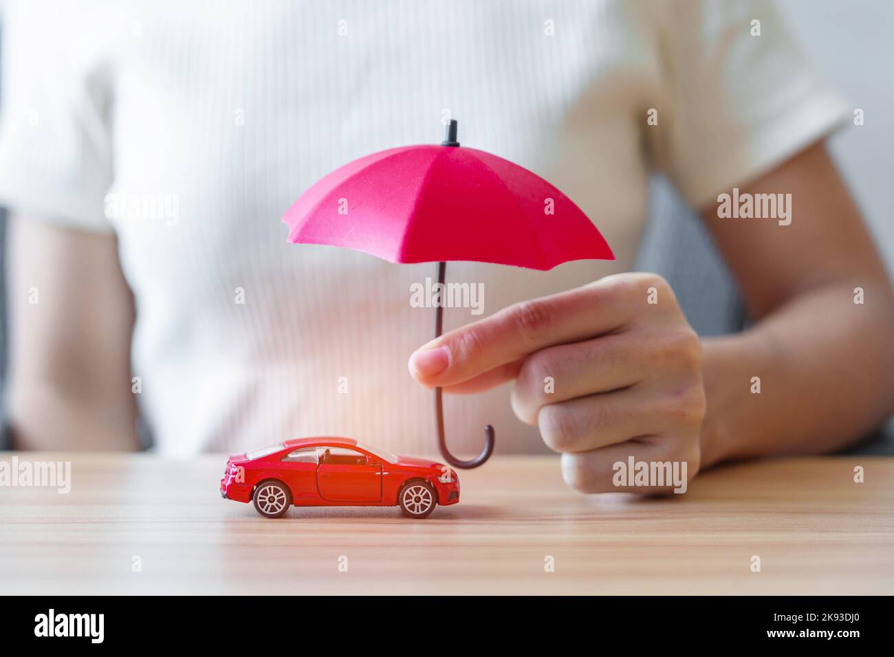 Businesswoman hand holding red umbrella and cover red car toy on table. Car insurance, warranty, repair, Financial, banking and money concept Stock Photo