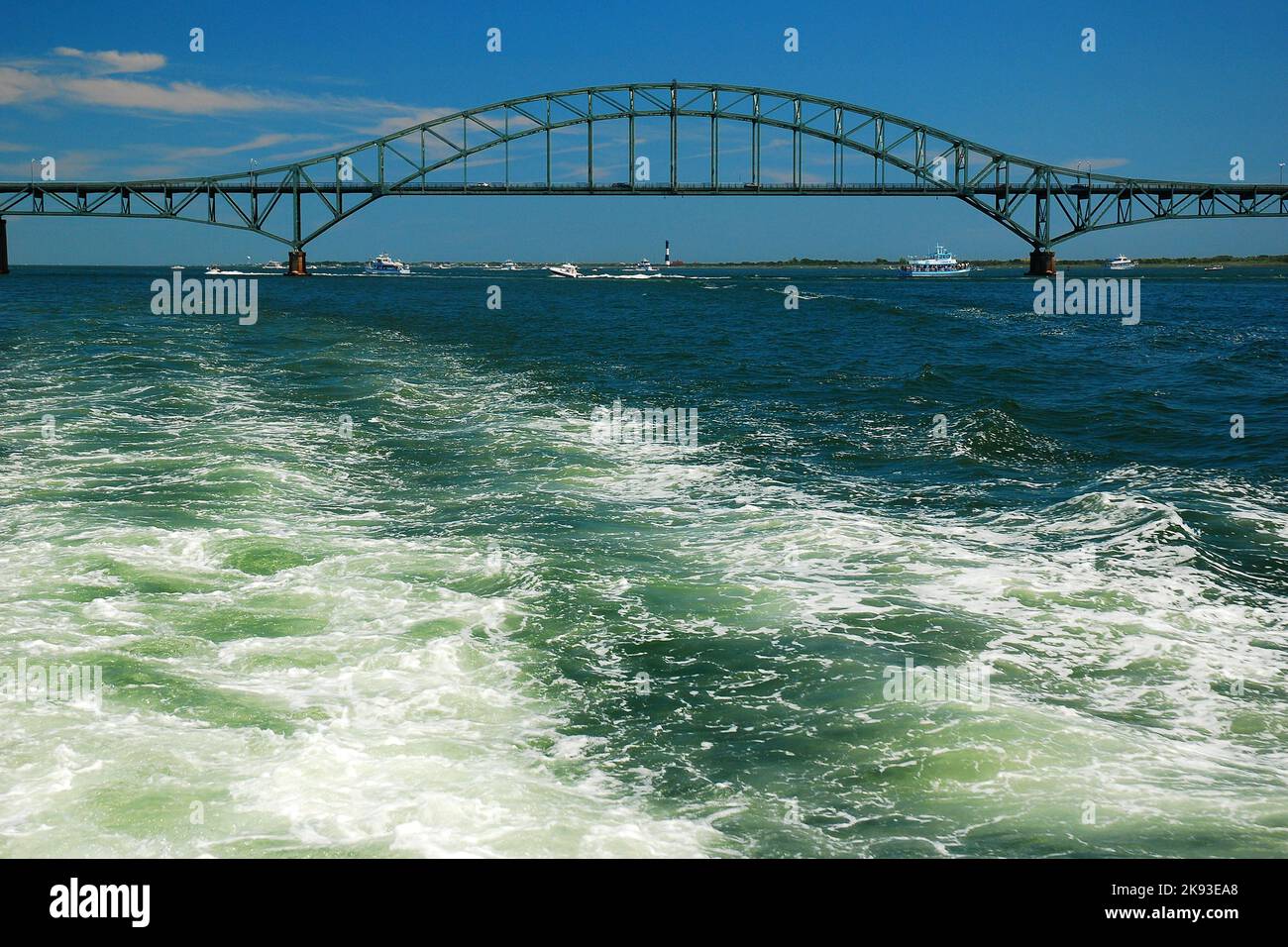 The wake of a boat in the bay pulls away from the steel arch bridge of the Robert Moses Causeway on Long Island Stock Photo