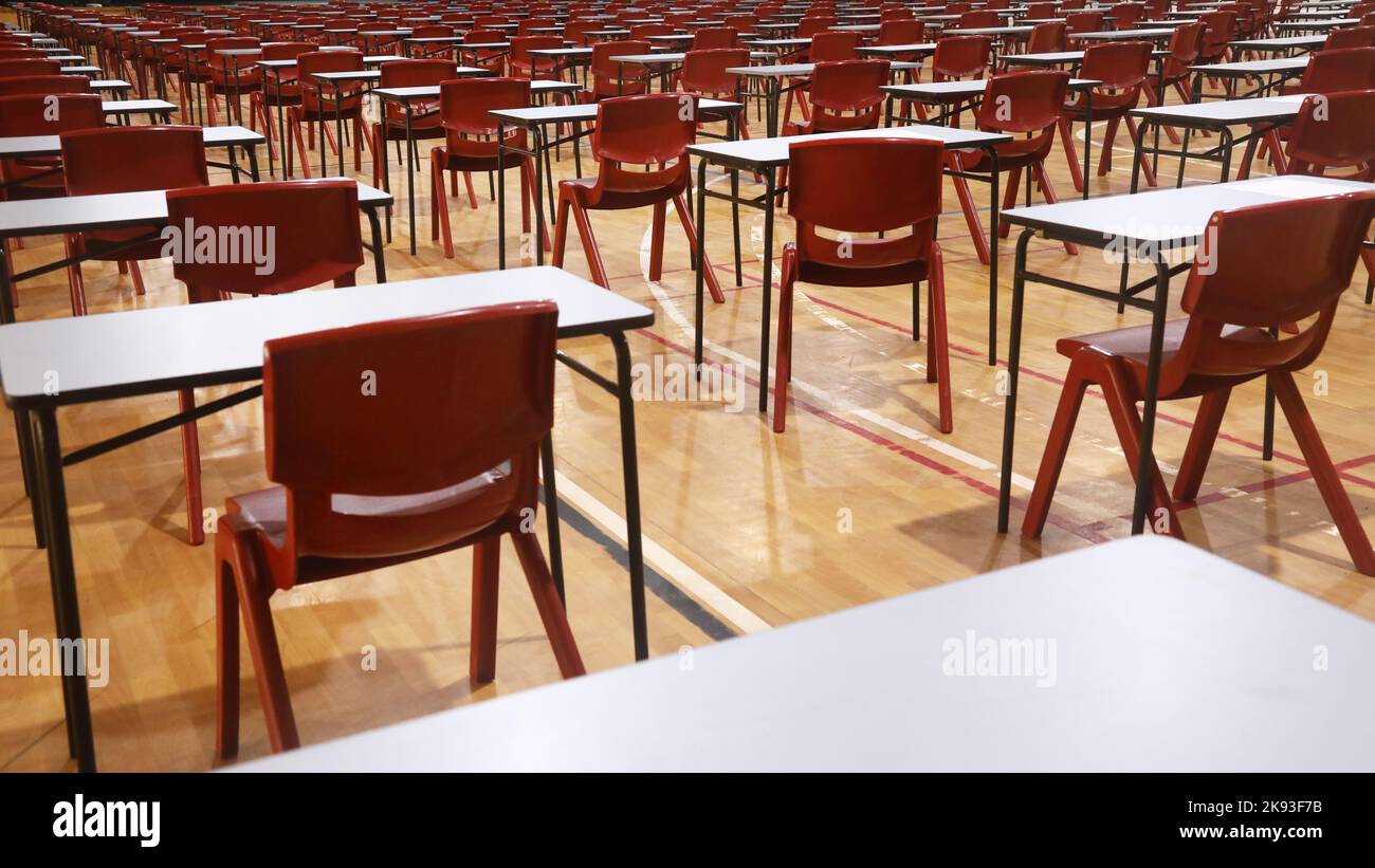 View of a secondary or high school student examination hall set up and organized in neat rows of exam tables or desks and red chairs. Stock Photo