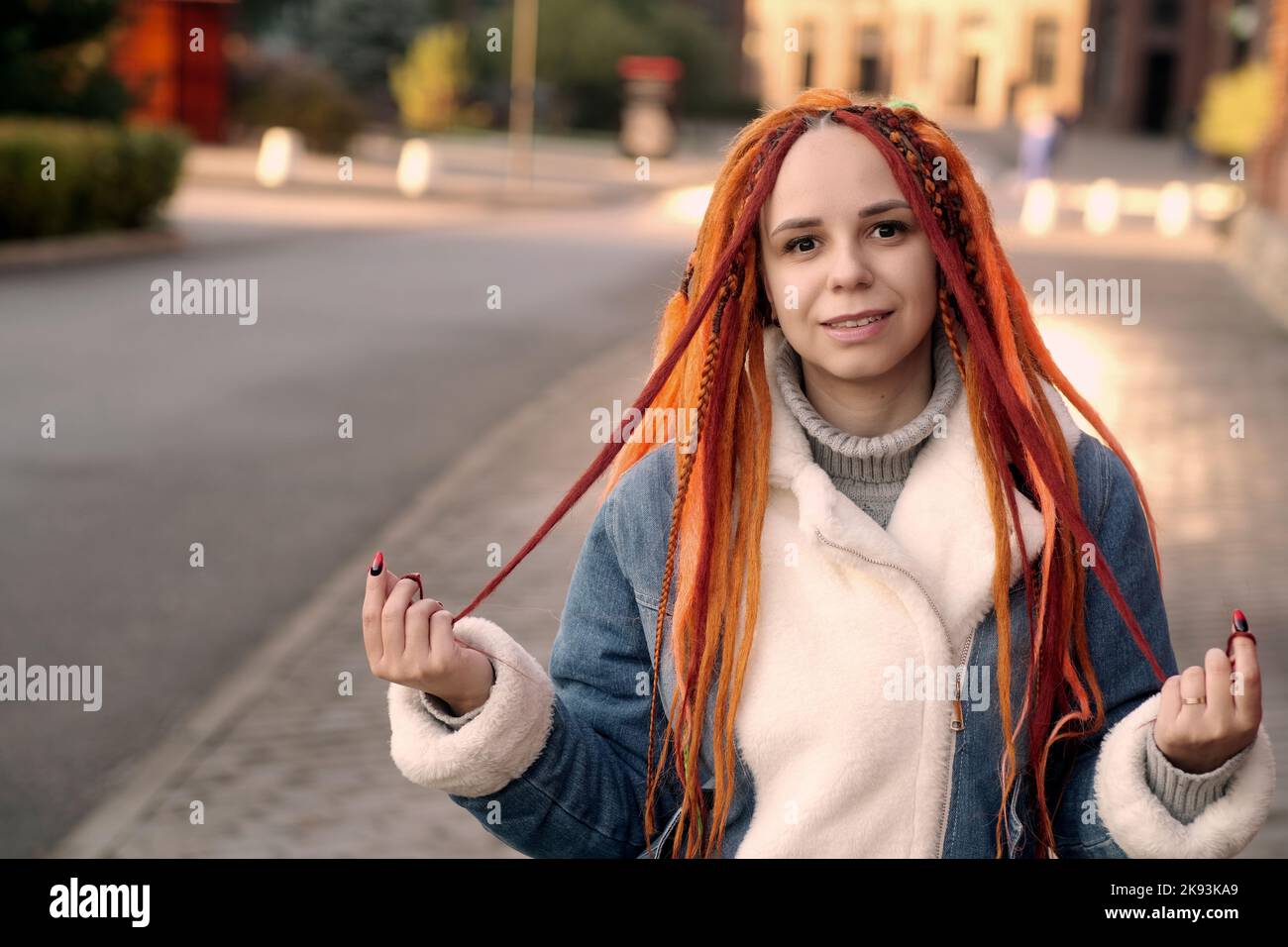 Portrait of young woman with ginger dreadlocks posing on city street