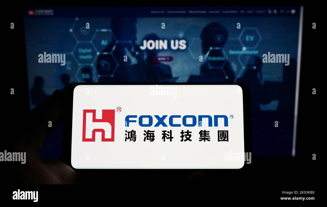 Person holding smartphone with logo of Hon Hai Precision Industry Co. Ltd. (Foxconn) on screen in front of website. Focus on phone display. Stock Photo