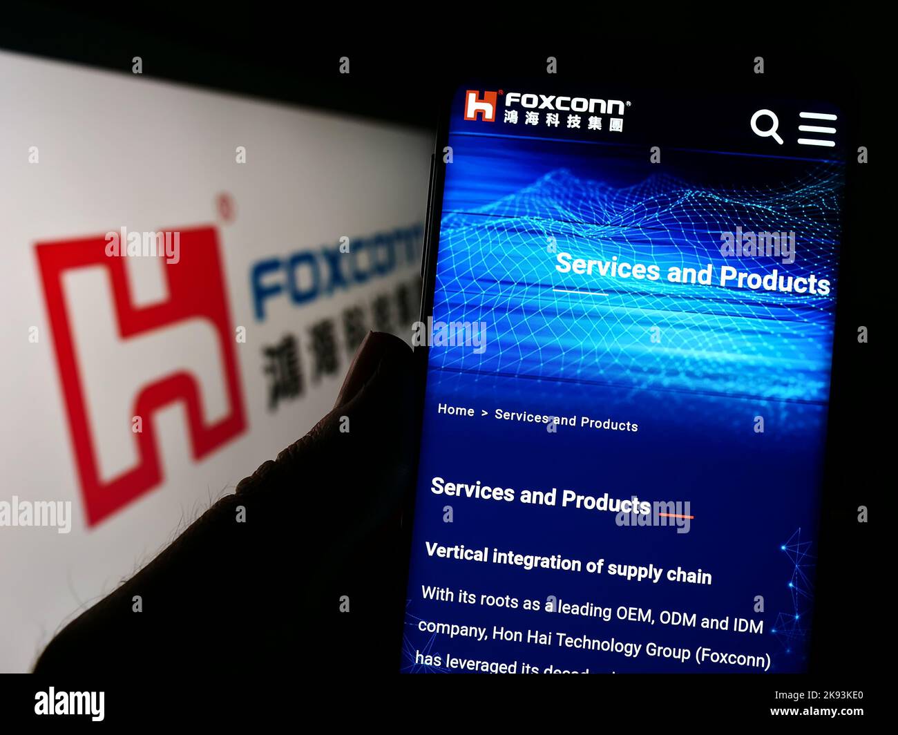 Person holding cellphone with webpage of Hon Hai Precision Industry Co. Ltd. (Foxconn) on screen with logo. Focus on center of phone display. Stock Photo