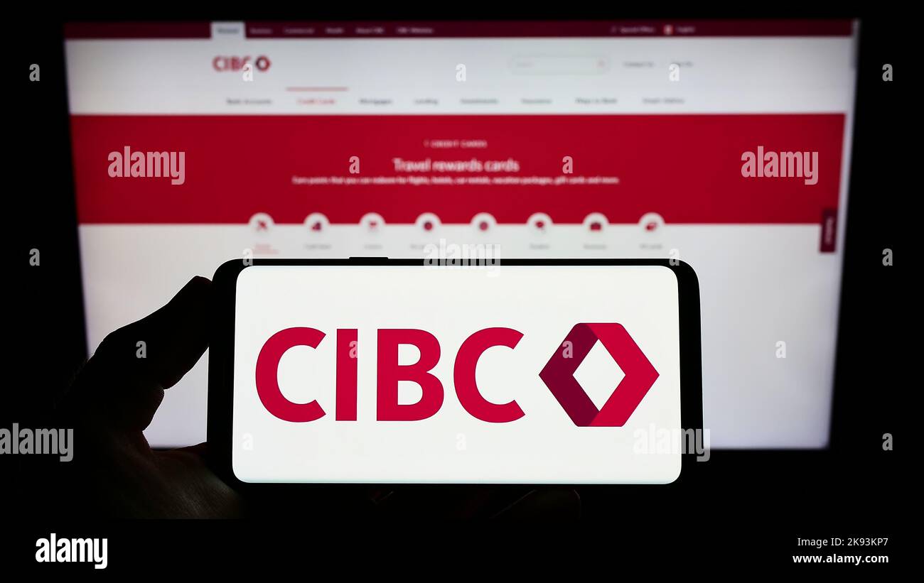 Person holding smartphone with logo of Canadian Imperial Bank of Commerce (CIBC) on screen in front of website. Focus on phone display. Stock Photo