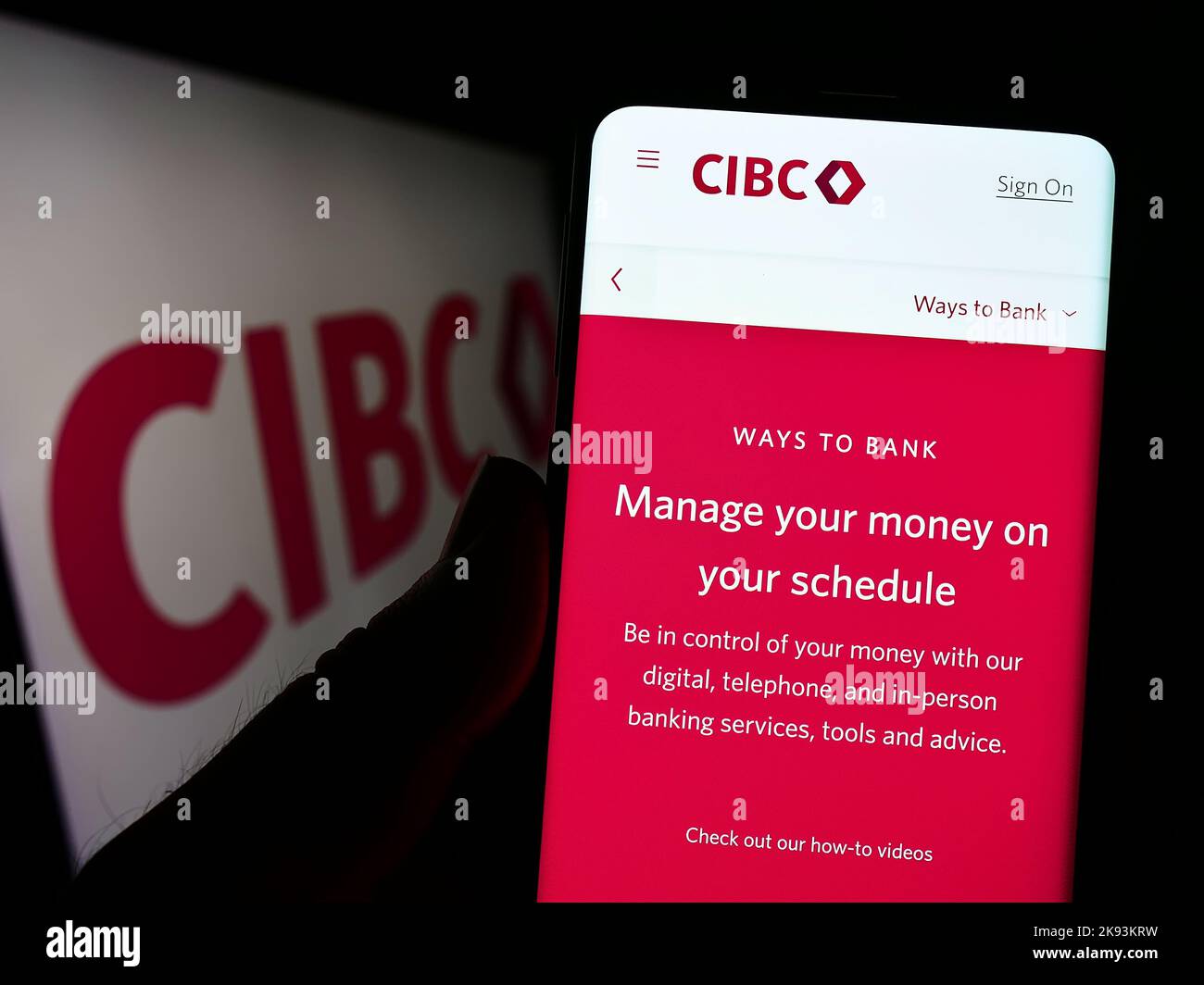 Person holding smartphone with website of Canadian Imperial Bank of Commerce (CIBC) on screen in front of logo. Focus on center of phone display. Stock Photo