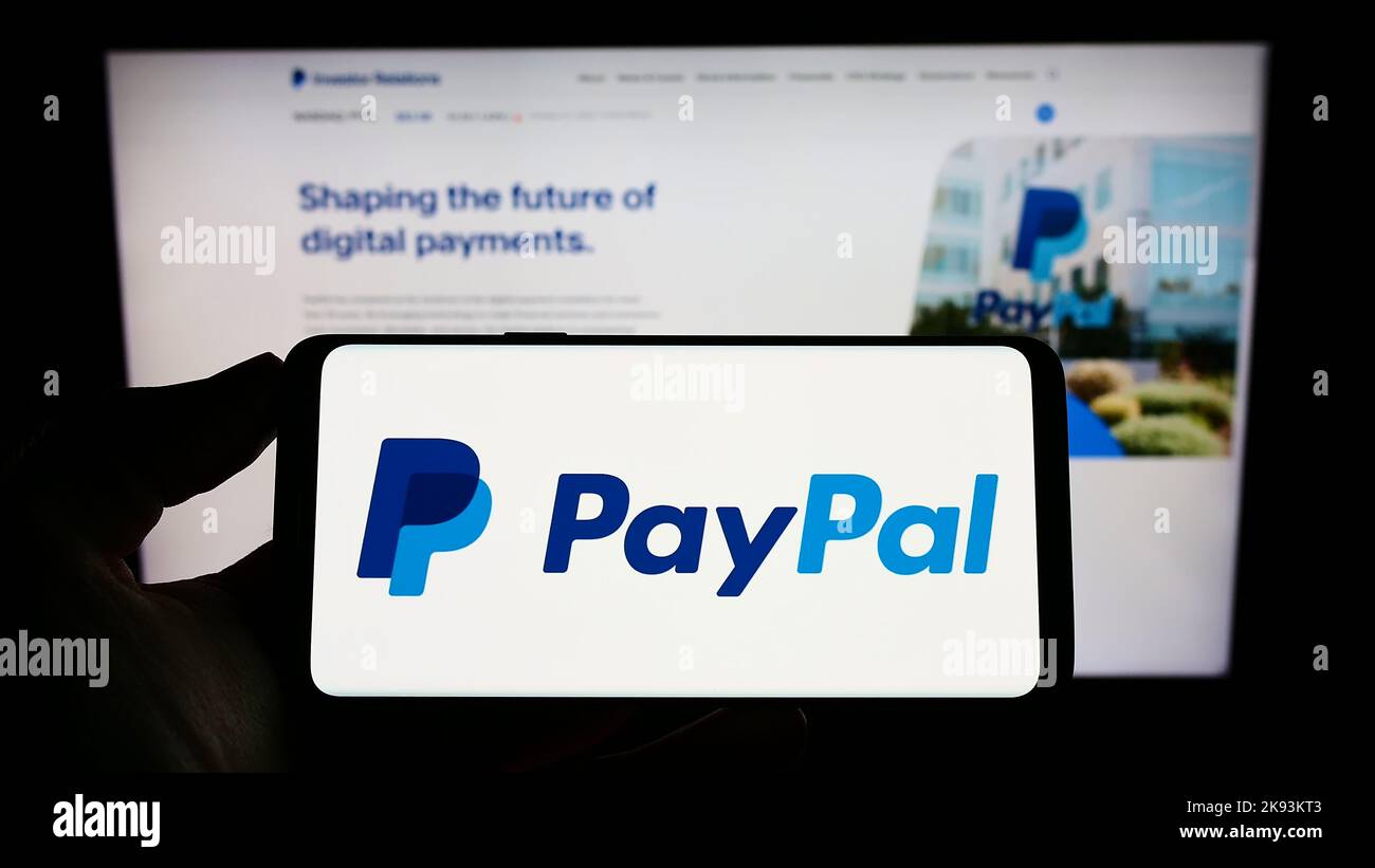 Person holding smartphone with logo of US financial company PayPal Holdings Inc. on screen in front of website. Focus on phone display. Stock Photo