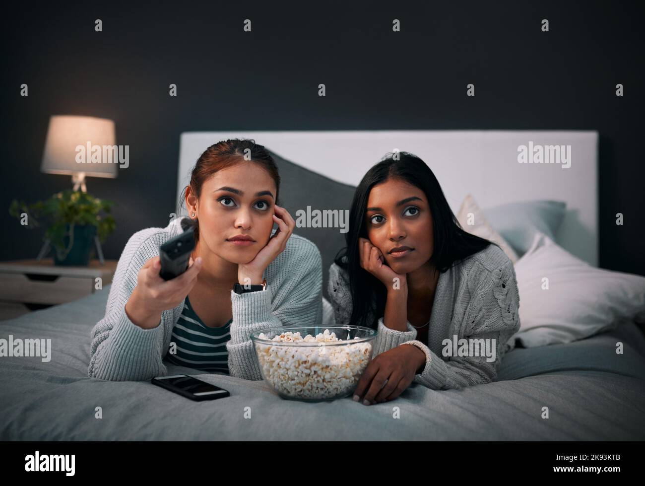 Not finding anything interesting to watch. two young women eating popcorn while watching a movie at home. Stock Photo