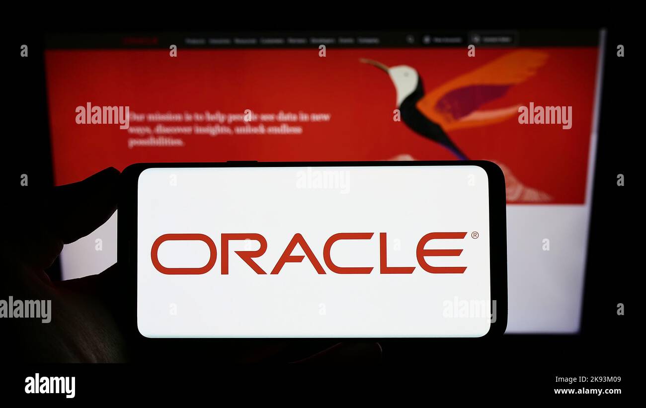 Person holding smartphone with logo of US technology company Oracle Corporation on screen in front of website. Focus on phone display. Stock Photo