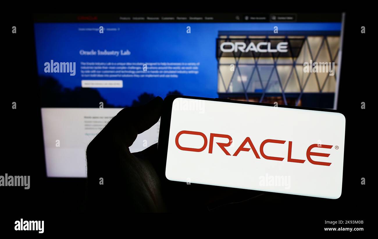 Person holding cellphone with logo of US technology company Oracle Corporation on screen in front of business webpage. Focus on phone display. Stock Photo