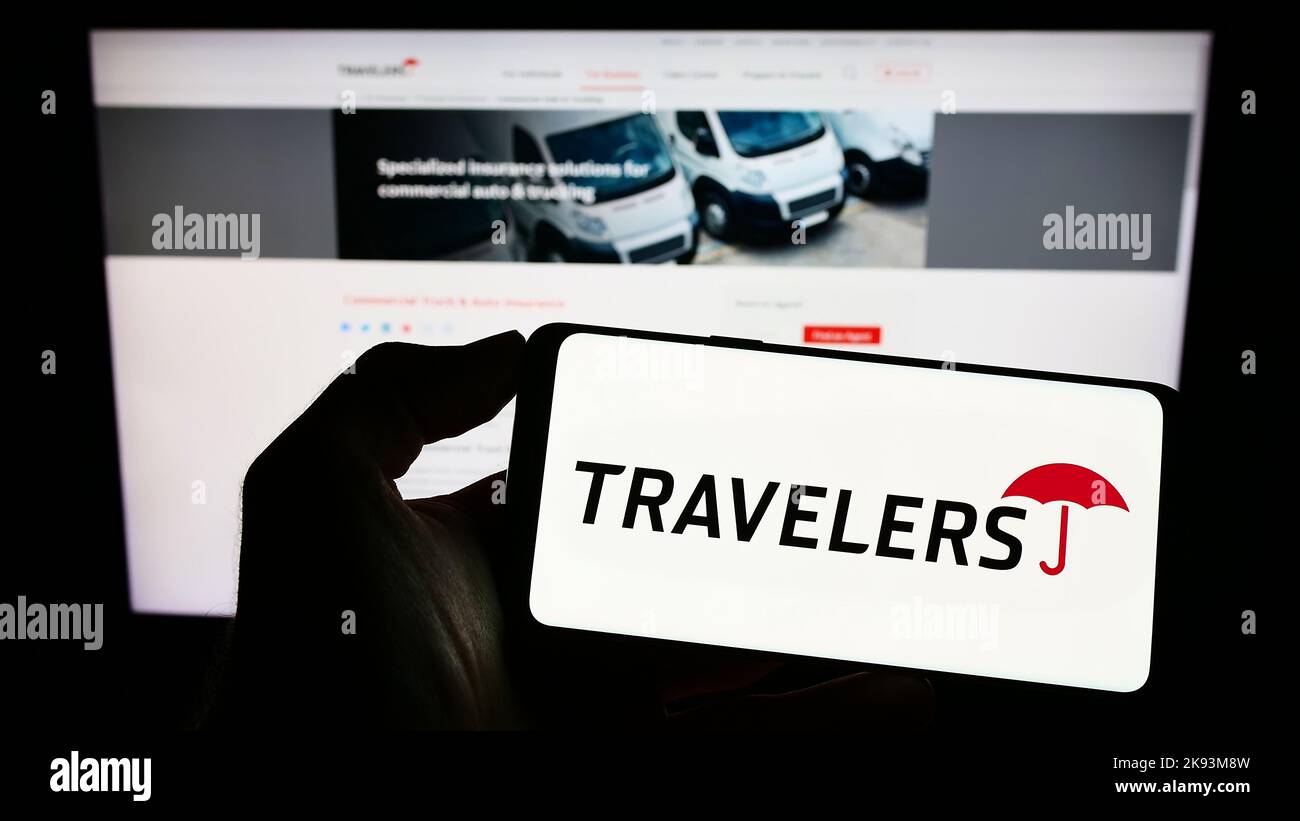 Person holding cellphone with logo of US insurance company The Travelers Companies Inc. on screen in front of webpage. Focus on phone display. Stock Photo