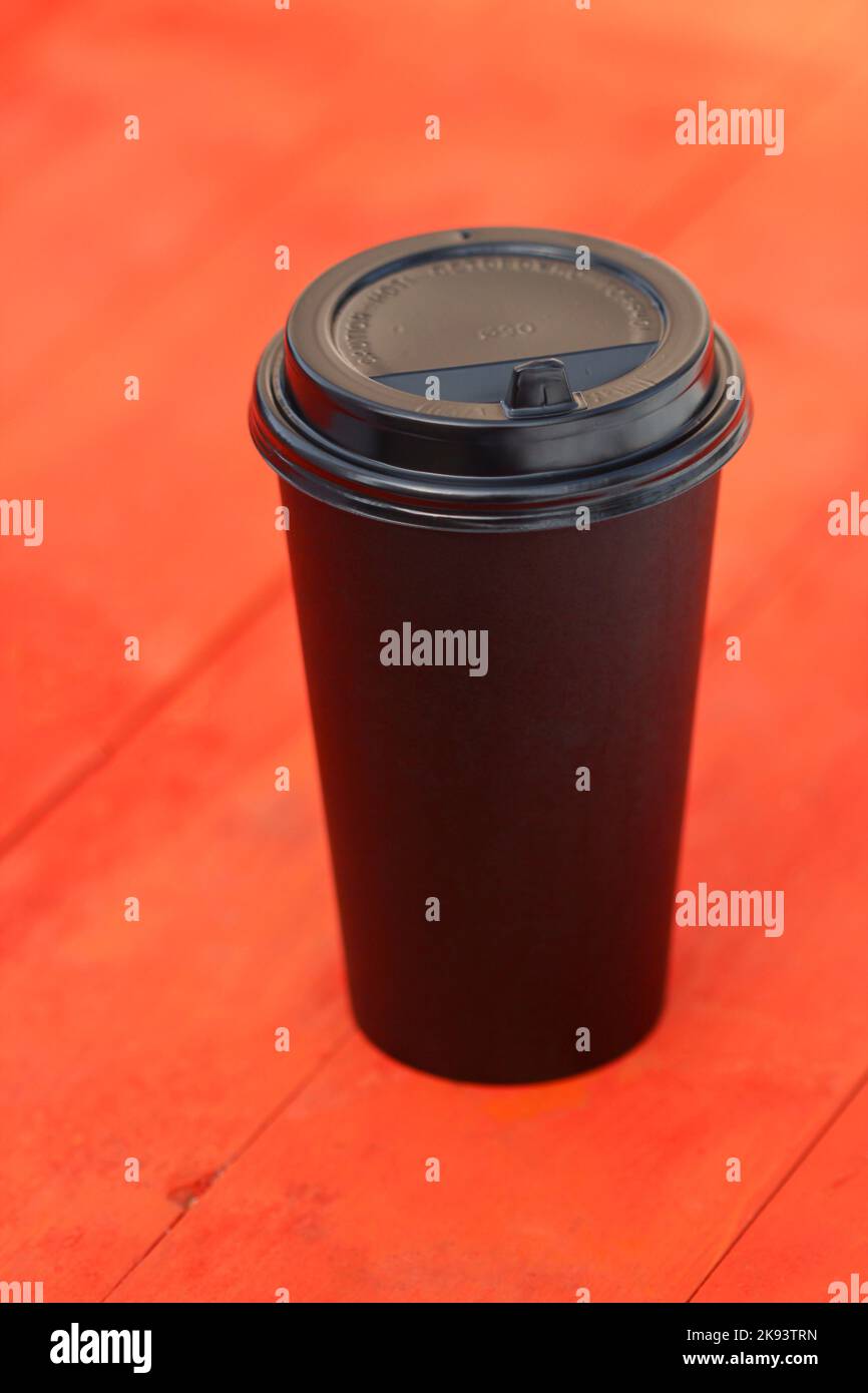 Disposable black plastic coffee cup on red wooden table Stock Photo