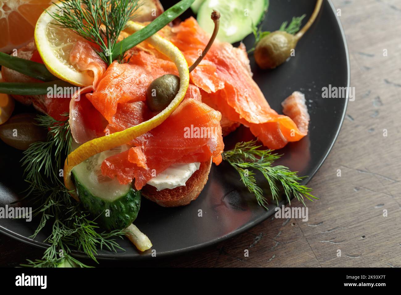 Sandwich with salmon, cream cheese, dill, cucumber, capers, green onion, and lemon. Stock Photo