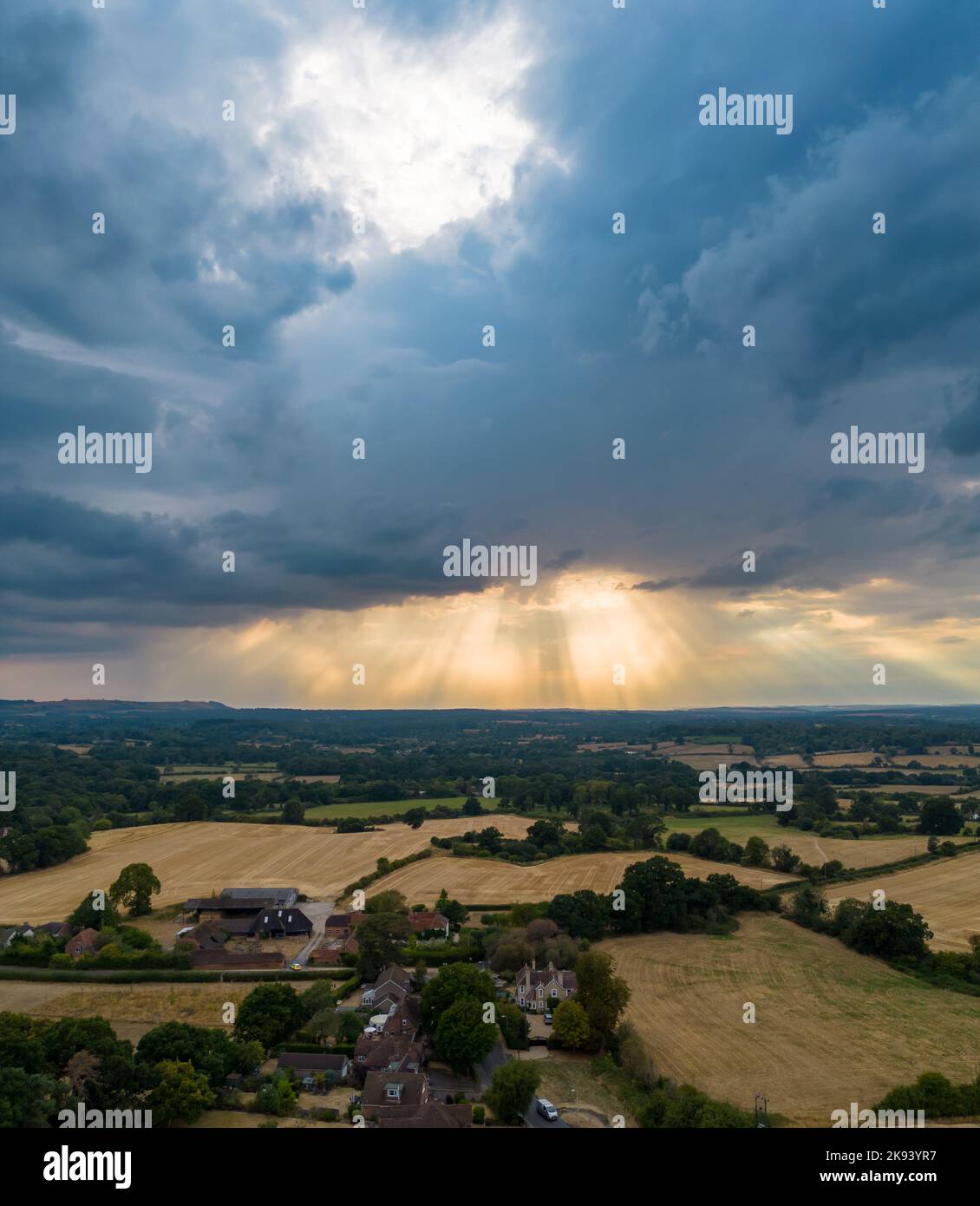 Stunning aerial landscape image of the sun’s rays shining through gap in clouds onto English countryside captured by drone in portrait mode Stock Photo
