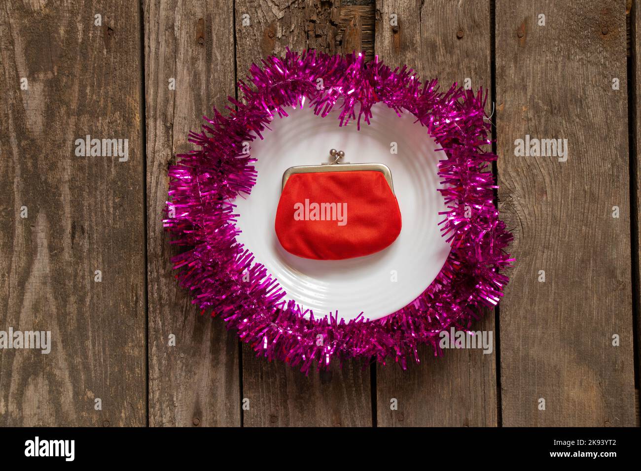 red wallet lies on a white plate decorated New Year's colored ribbon on a wooden background close-up, New Year's decor Stock Photo