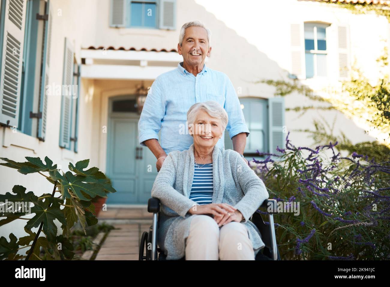 We stuck together through thick and thin. Portrait of a cheerful wheelchair bound senior woman relaxing with her husband in their backyard at home. Stock Photo