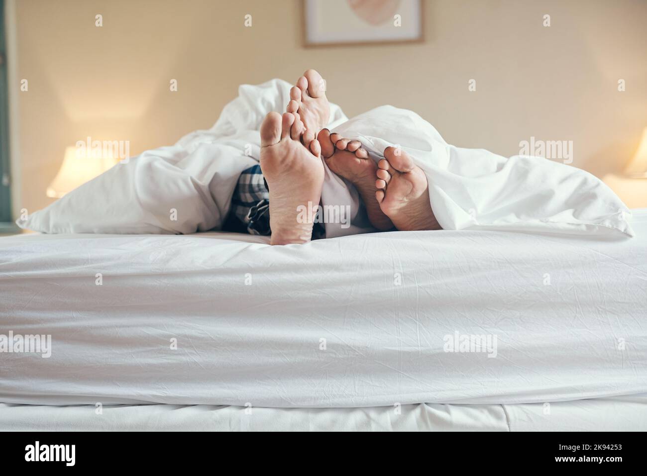 Lets stay in bed for the rest of day. an unrecognizable couples feet poking out under the sheets