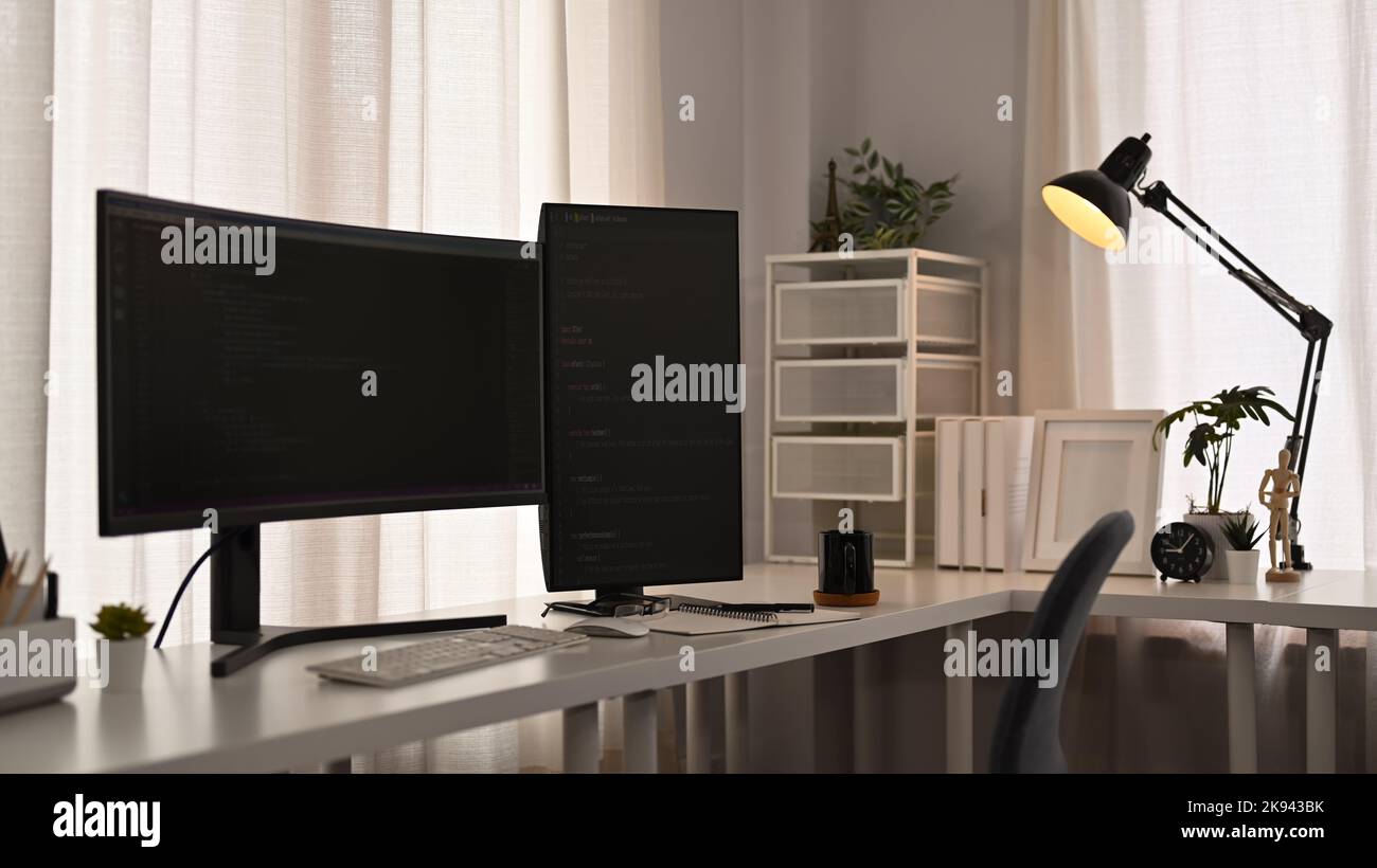 Computer monitors with coded data, supplies on wooden table in software development office Stock Photo