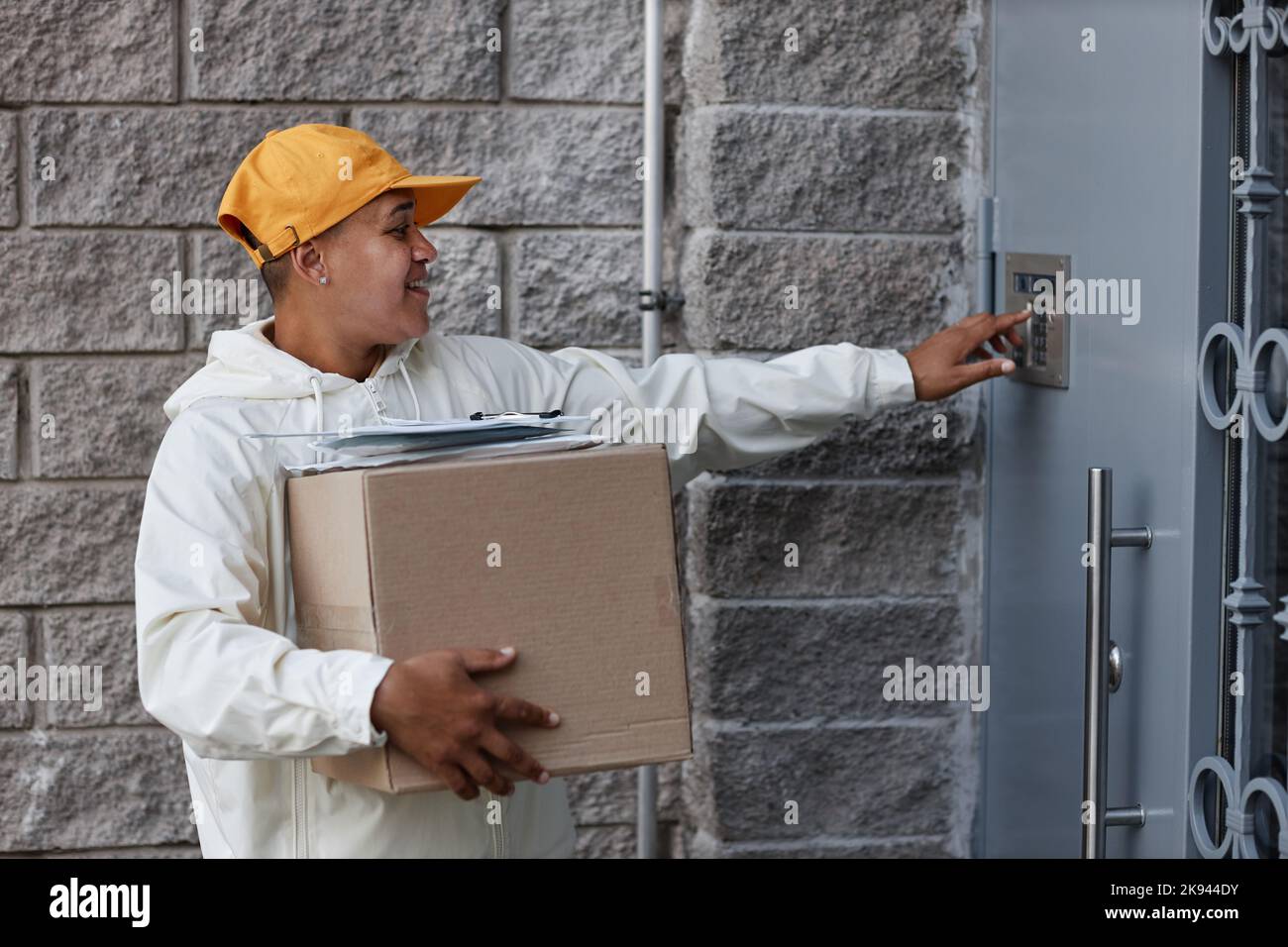 Side view portrait of multiethnic young woman delivering packages and ringing doorbell Stock Photo