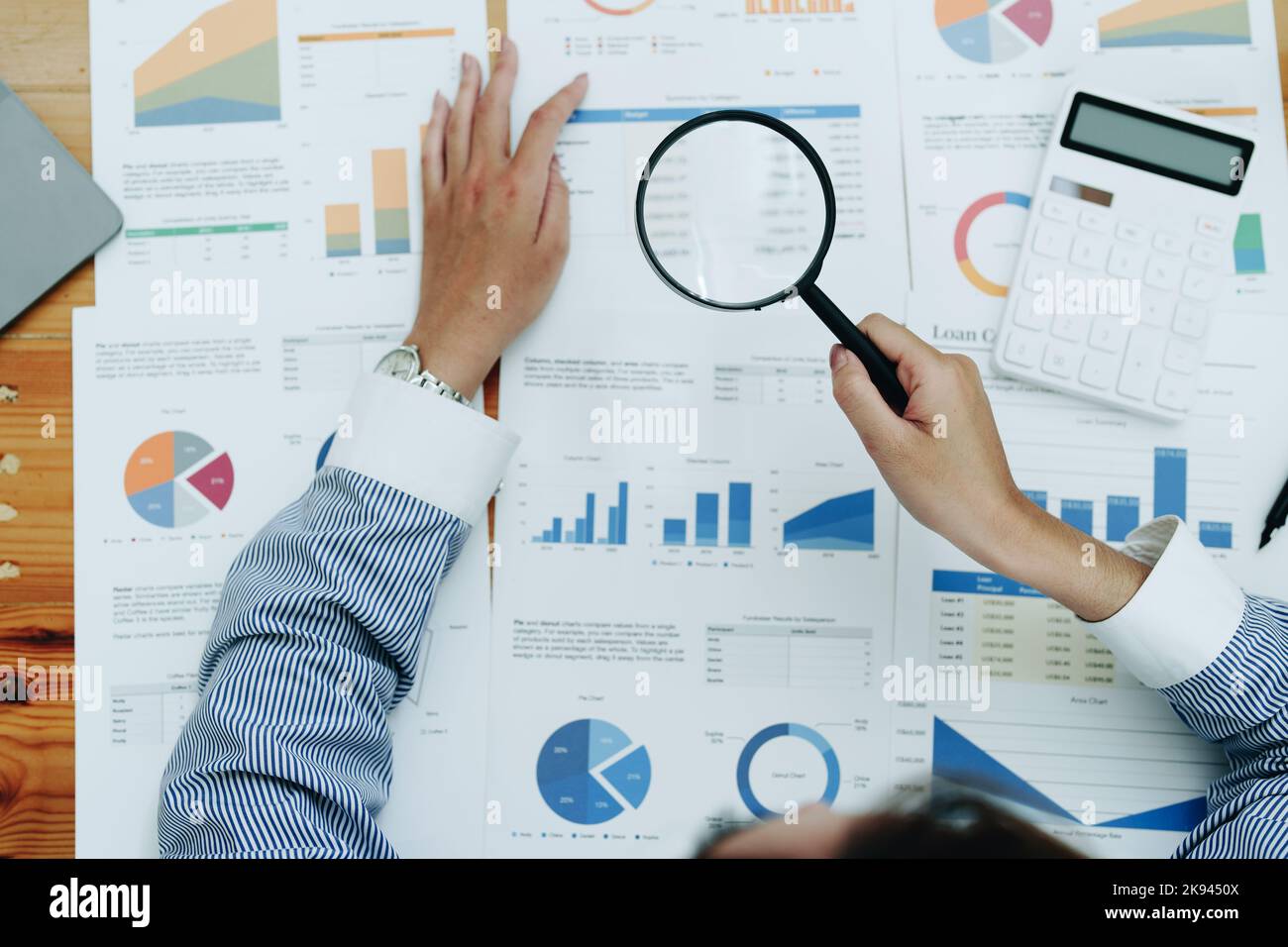 Financial analysts analyzing business financial reports are examining documents using a magnifying glass as a working concept Stock Photo