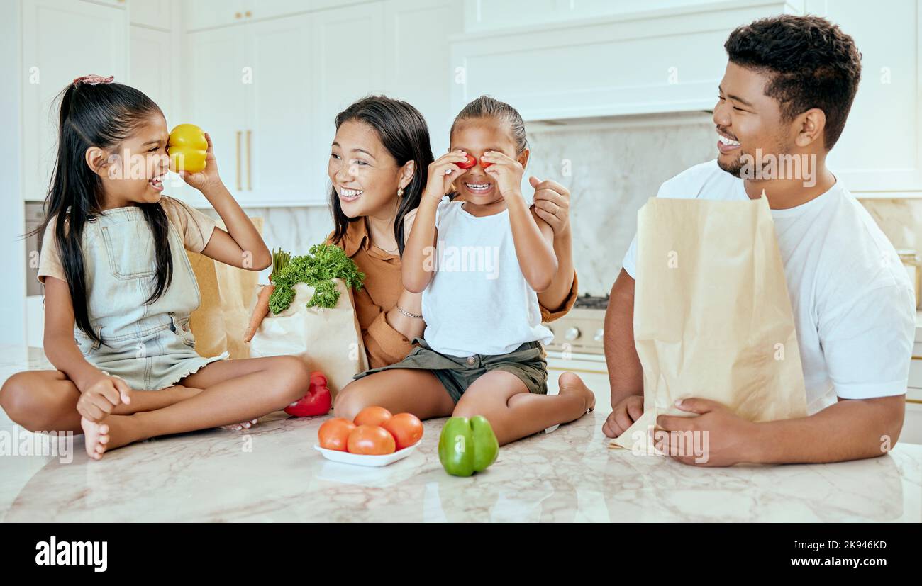 Asian, vegetables and family in kitchen for playing at table, happy or together for bonding. Mom, dad and children with smile at counter for health Stock Photo