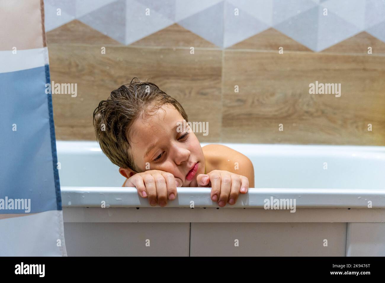 boy is sitting in bath with water with his head on the edge of the tub Stock Photo Alamy