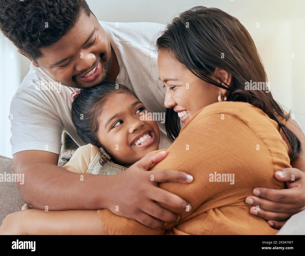 Asian family, parents and child hug on sofa bonding, love and affection in family home. Indian father, mother and girl relax together loving embrace Stock Photo