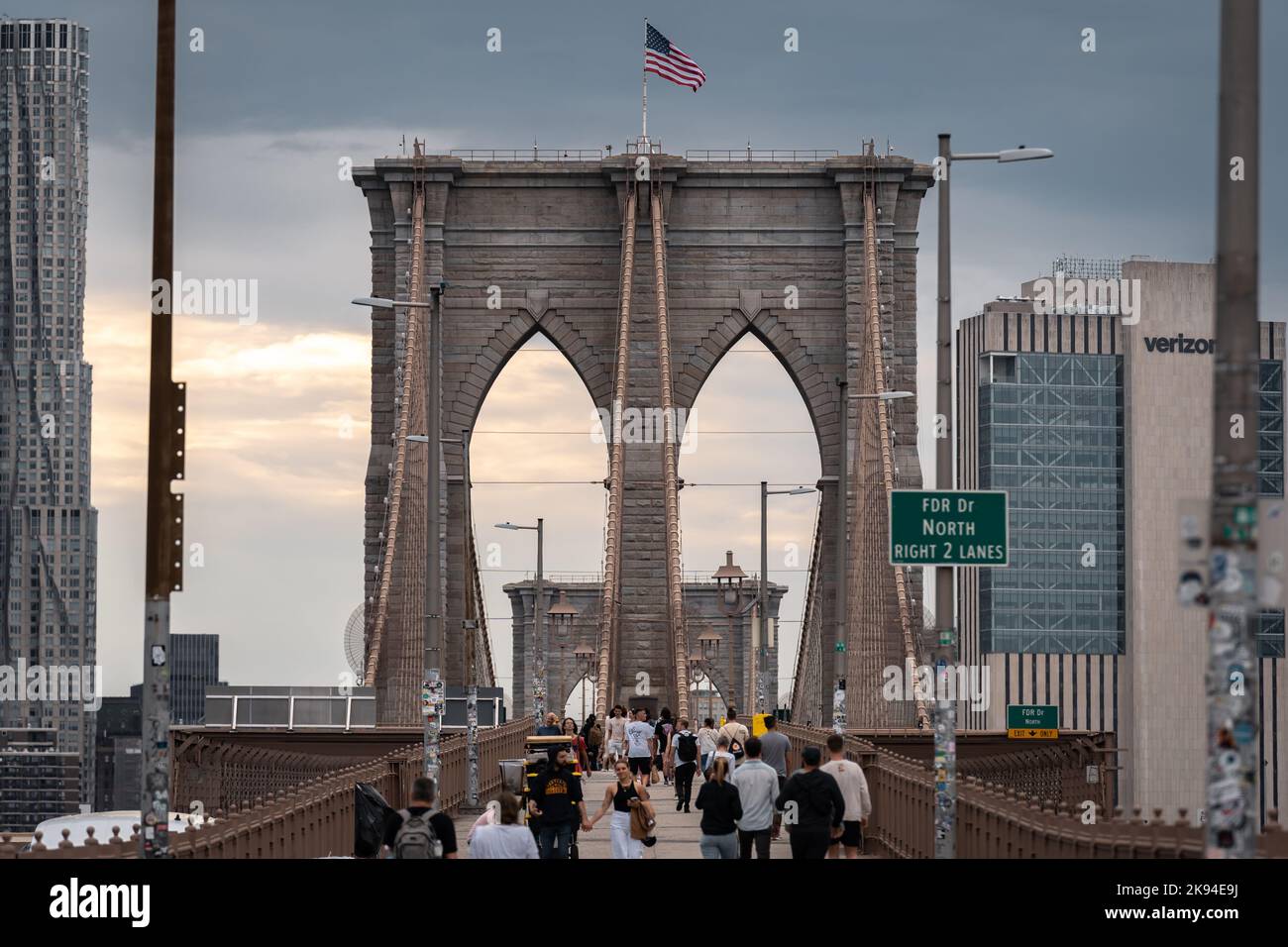 The people walking along Brooklyn bridge with the American flag on its top Stock Photo
