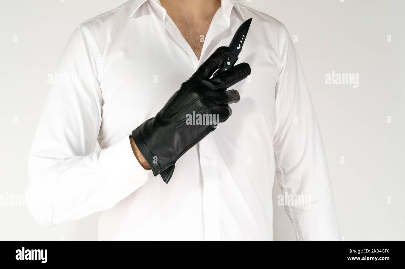 White guy with shirt and black glove holding knife hand on white background. Men hold knife with leaher glove. Killer, psycho, mafia or gangster Stock Photo