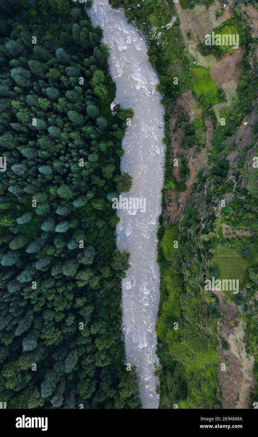 An aerial top view of a river flowing through green forests and fields ...