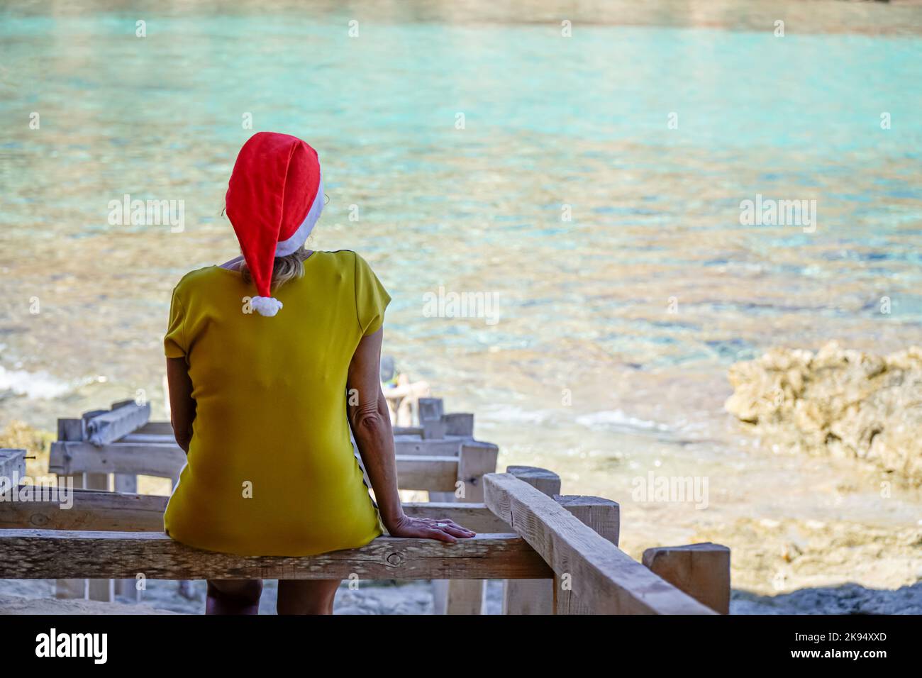 older woman with santa claus hat on the coast looking at the sea ...