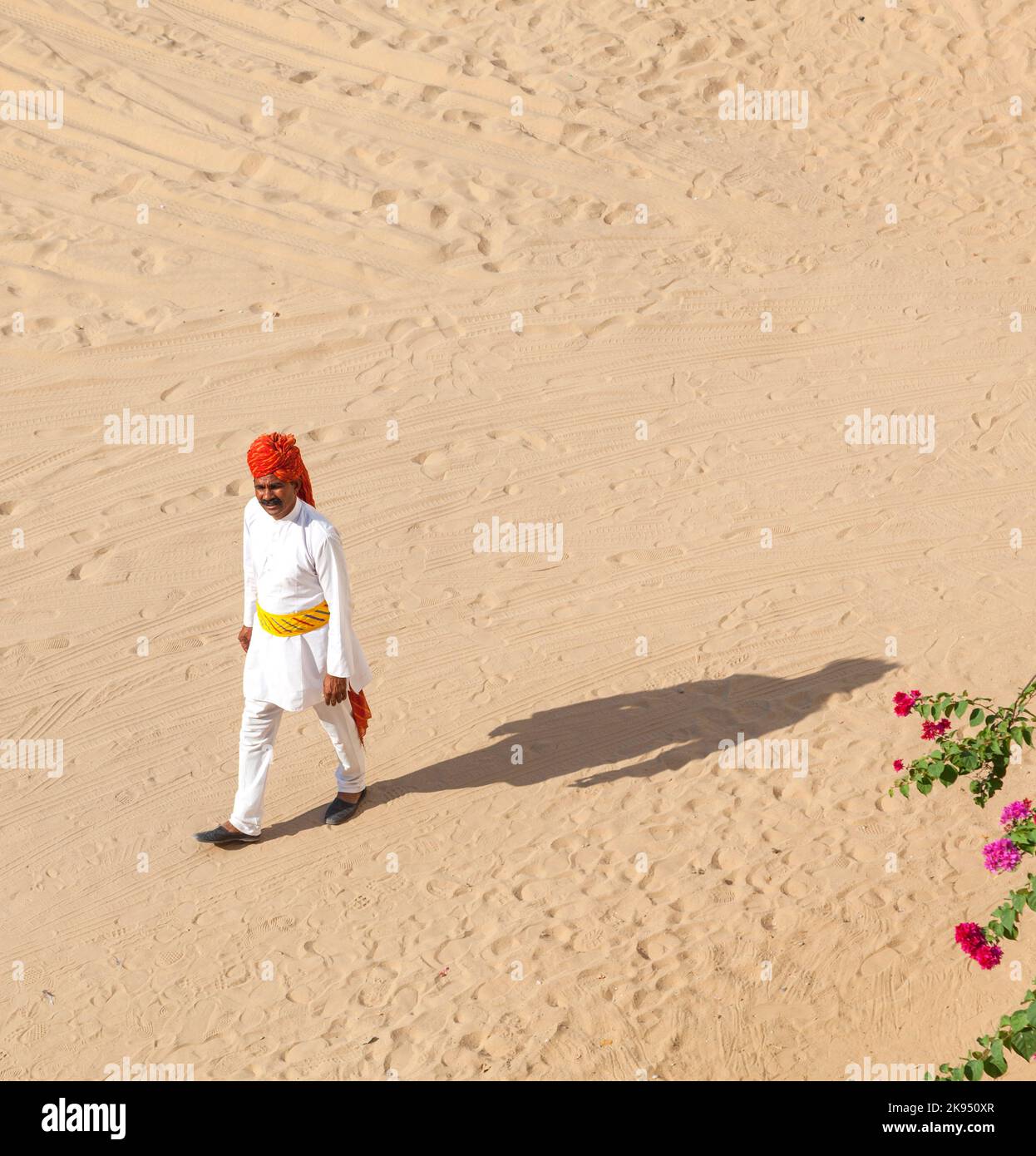 Mandawa, India - October 25, 2012: A Rajasthani waiter wearing traditional colorful turban passes the empty parking lot at the desert hotel  in Pushka Stock Photo