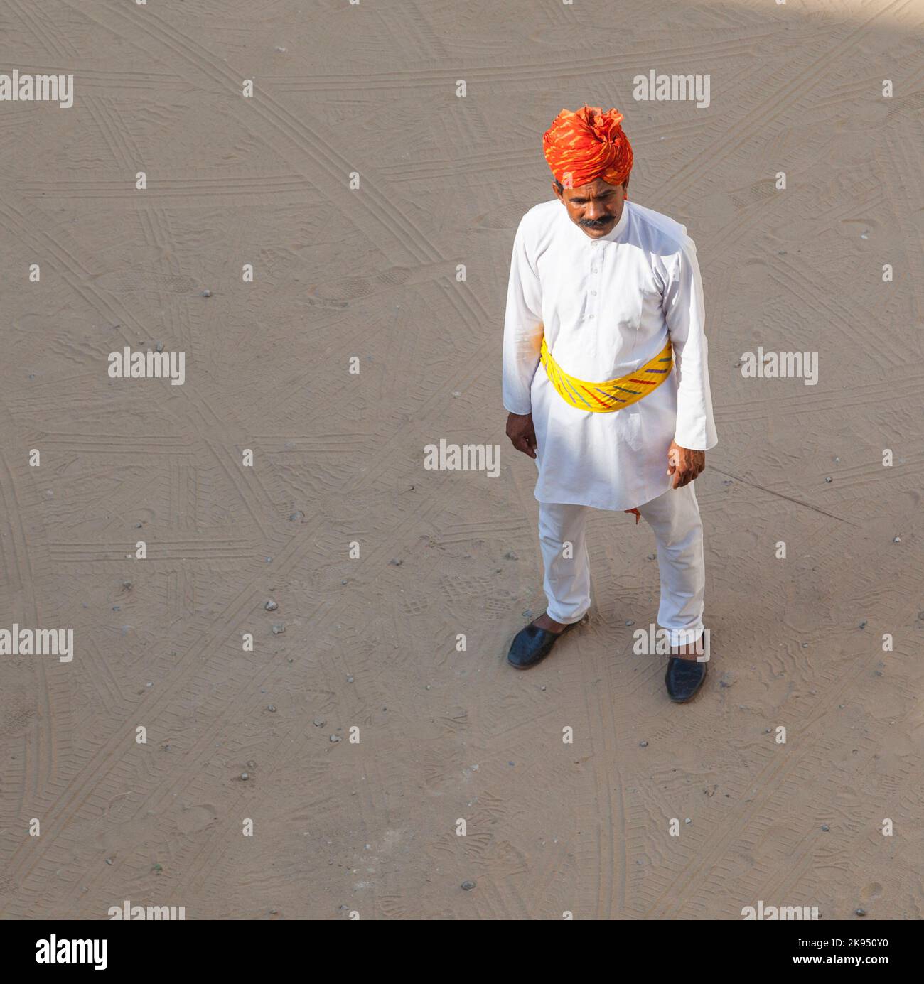 Mandawi, India - October 25, 2012:  A Rajasthani waiter wearing traditional colorful turban passes the empty parking lot at the desert hotel in Pushka Stock Photo